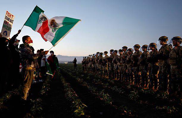 Migrantes ondean bandera de México frente a militares estadounidenses en acto de protesta